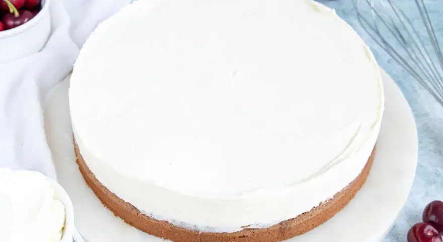 Ein köstlicher Kuchen mit Mascarpone-Creme, garniert mit frischen Kirschen und einem Schneebesen daneben.