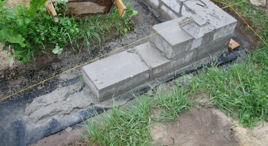Fundamenty z betonu i bloczków, częściowo zalane, otoczone trawą. Pytanie, czy można zostawić odkryte fundamenty na zimę, jest tu kluczowe.
