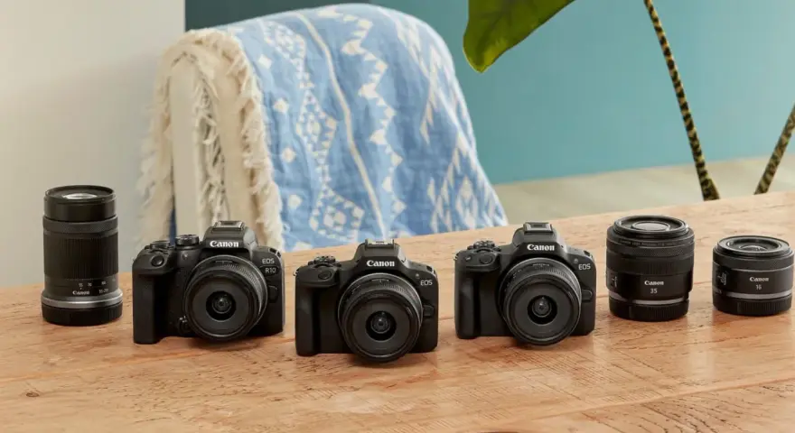 Trzy czarne aparaty Canon EOS z obiektywami i dodatkowe obiektywy na drewnianym stole.