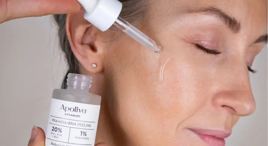 Droppe av aha-syra ansikte-serum appliceras på huden. En flaska med peeling syns i förgrunden.