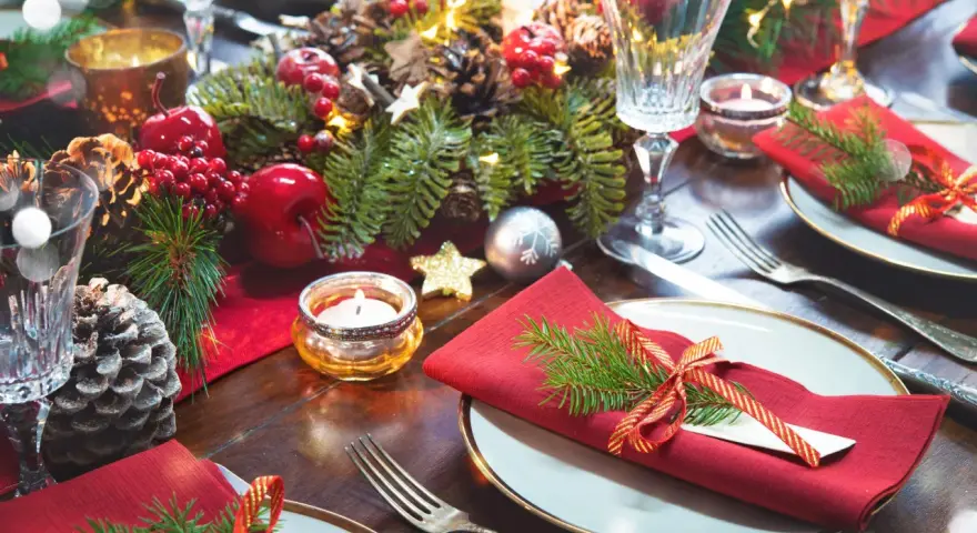 Vackert dukat julbord med röda servetter, granris, äpplen, kottar och ljus. Här ser du vad man har på ett julbord för att skapa julstämning.