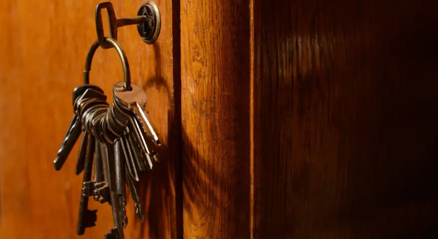 Un trousseau de clés pend à une serrure sur une porte en bois. Ces clés symbolisent la sécurité et la protection, rappelant les lois anti squat.