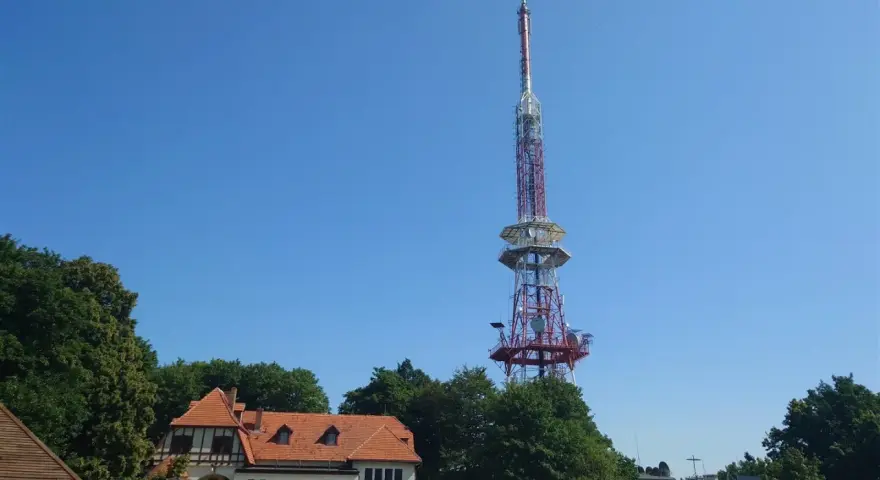 Wieża widokowa na górze Ślęża góruje nad budynkiem schroniska i zielonymi drzewami.