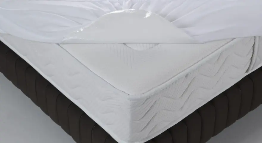 Un matelas blanc avec une alèse imperméable soulevée, montrant de quel côté mettre une alèse pour protéger le matelas.