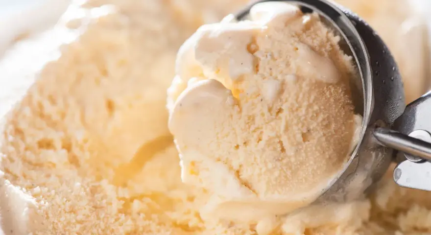 Ein Löffel nimmt eine Kugel cremiges Eis auf. Kleine eiskristalle im eis glitzern im Licht.