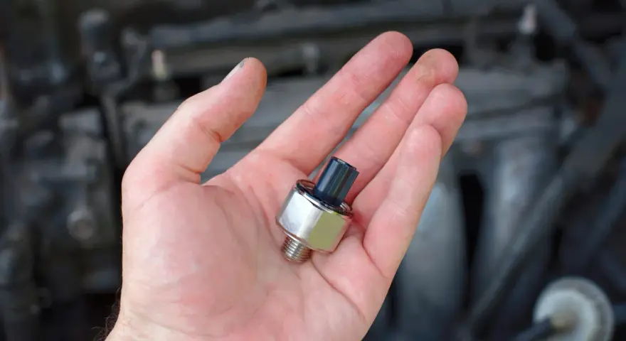 A hand holds a new oil pressure sensor, a potential fix for a p0332 code Chevy Silverado.