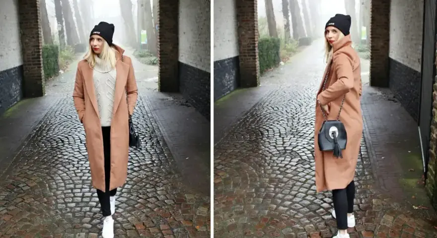 Kobieta w płaszczu w kolorze camel i czarnej czapce idzie brukowaną alejką.