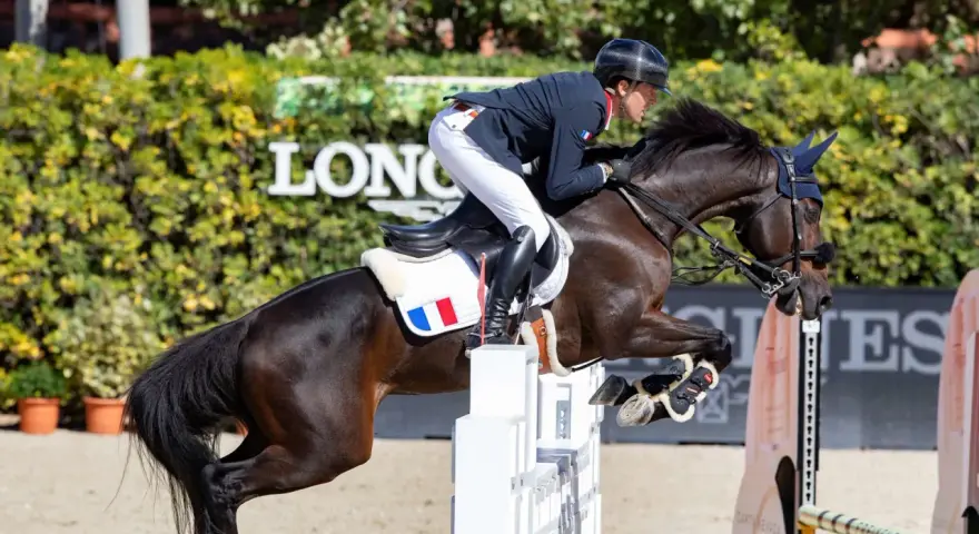 Cavalier français en plein saut lors d'un concours hippique. Le cheval, puissant et concentré, franchit un obstacle blanc.