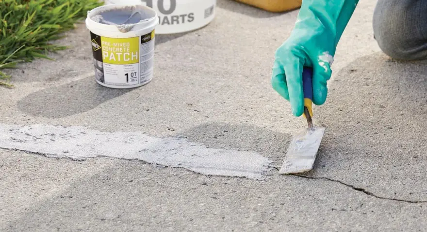 Applying pre-mixed concrete patch to fix cracks in pavement. A gloved hand uses a trowel to smooth the patch.