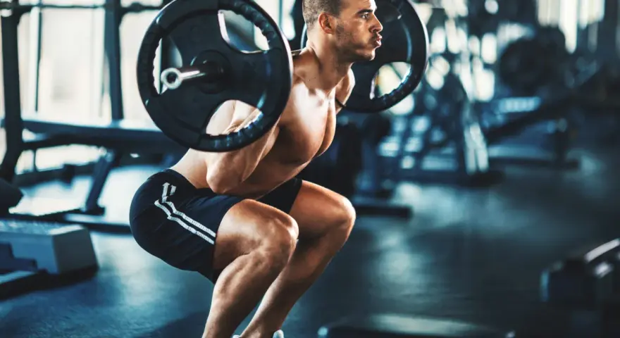 Man gör ett tungt benspark hemma med skivstång på axlarna i ett gym.