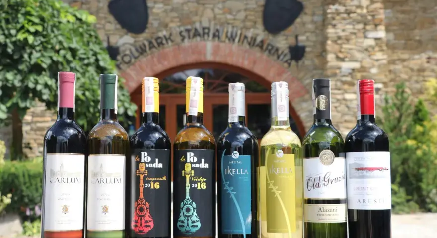 Wybierasz jakie wino na wesele? Rząd butelek z winem czerwonym i białym przed starą winnicą.