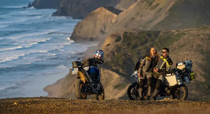 Para motocyklistów odpoczywa na klifie, podziwiając dzikie wybrzeże Algarve. Ich motocykle gotowe do dalszej podróży.