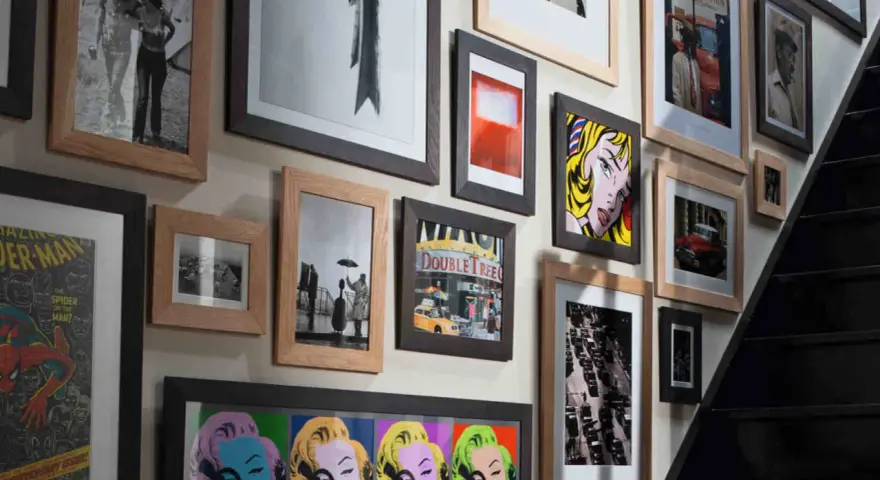 Un mur couvert de tableaux, dont des portraits de Marilyn Monroe, une scène de rue et une affiche de Spider-Man, le tout dans un cadre.