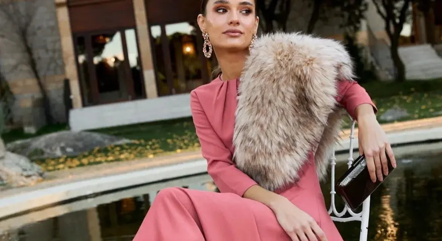 Elegante outfit fiesta invierno: vestido rosa palo, chal de pelo y bolso de mano.