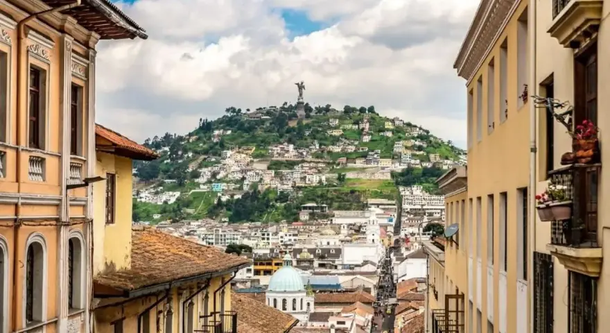 Widok na wzgórze z pomnikiem w Quito, stolicy Ekwadoru. Kolorowe budynki i wąskie uliczki tworzą malowniczy krajobraz.