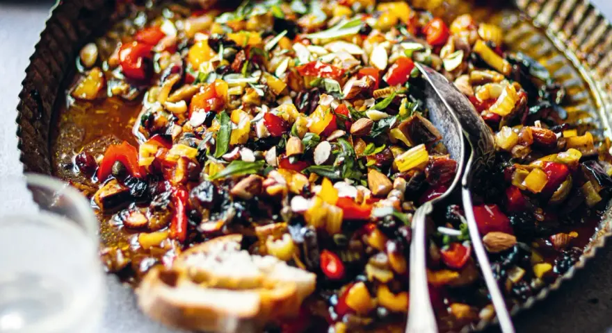 Pyszna caponata z selera z migdałami i oliwkami, podana w metalowej misie z pieczywem.
