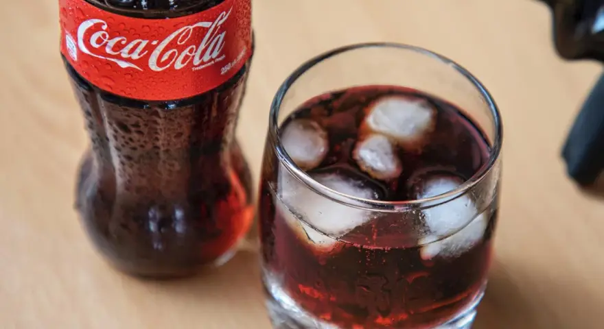 Szklanka z lodem i napojem, obok butelka Coca-Coli. Idealne na gorący dzień, gdy masz ochotę na wino z colą.