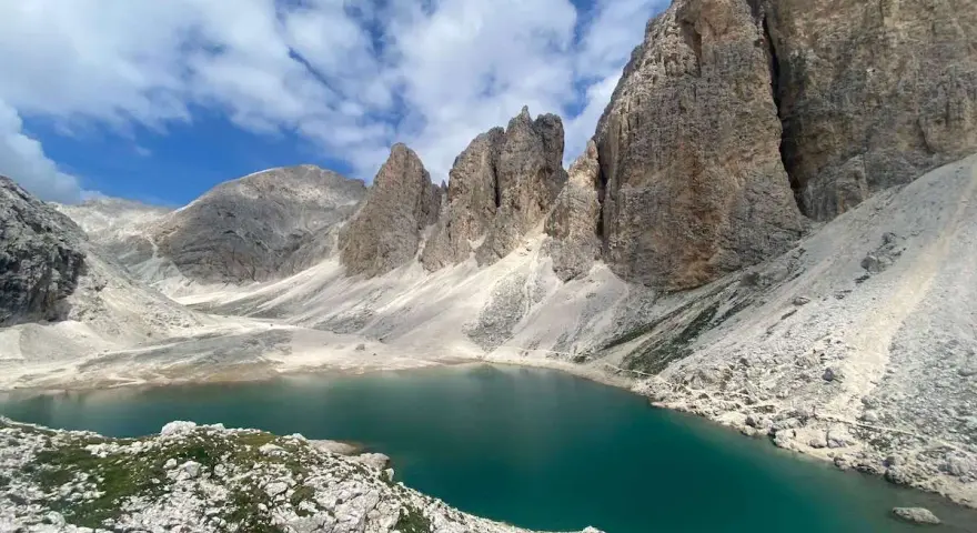 Il **lago di Antermoia**, incastonato tra imponenti vette rocciose, riflette il cielo azzurro e le nuvole bianche. Un gioiello alpino.