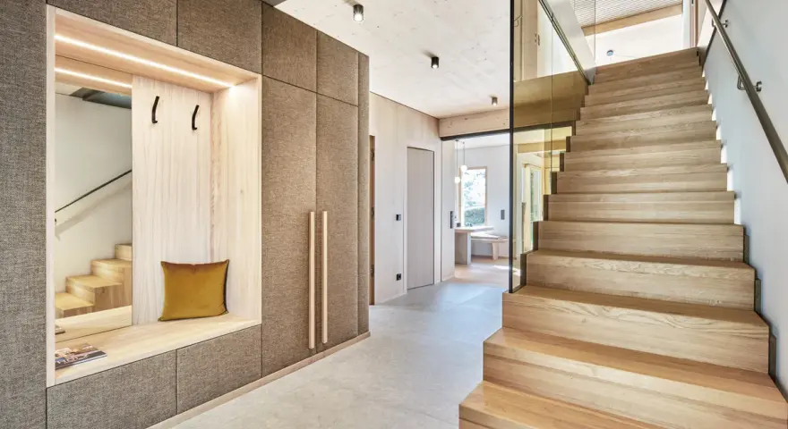 Moderne Diele mit Sitzbank und Garderobe, die Treppe aus verschiedenen **Hartholzarten** strahlt Wärme aus.