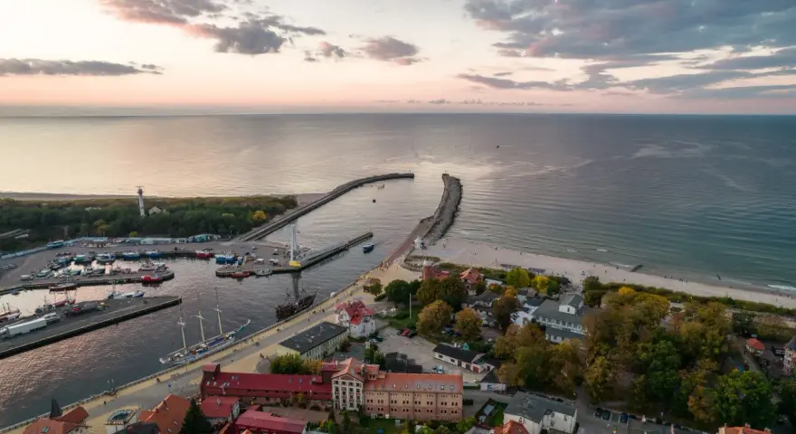 Widok z lotu ptaka na port w Ustce z łodziami i latarnią morską w tle.