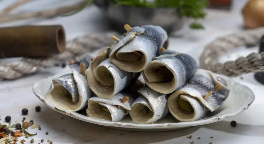 Gestapelte Rollmops Fisch auf einem Teller, garniert mit Gewürzen und Holzspießen.