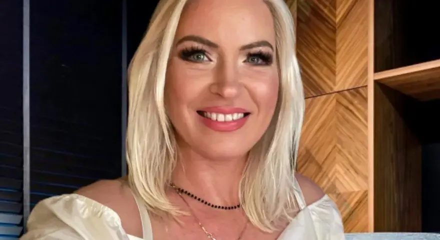 Uśmiechnięta Joanna Janikowska-Samojłowicz w białej bluzce z odkrytymi ramionami, z naszyjnikami na szyi.