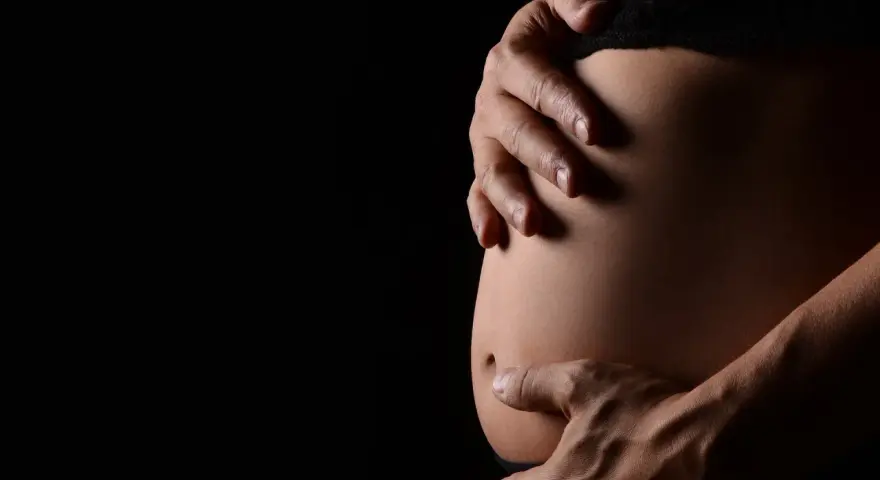 Mani che accarezzano un pancione. La ricerca sulle cause dell'autismo in gravidanza è complessa e in continua evoluzione.