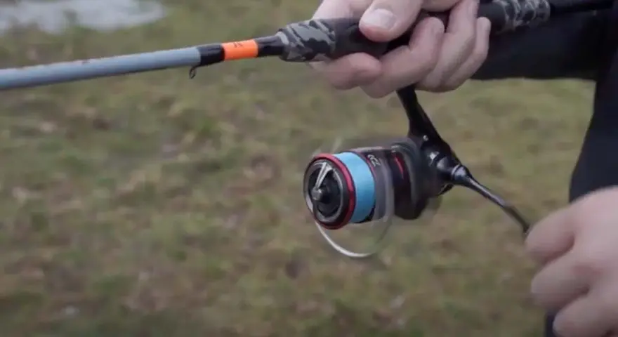 Daiwa Fuego Camo Spin Test: Eine Hand hält eine Angelrute mit Camo-Griff und einer Rolle mit blauer Schnur.