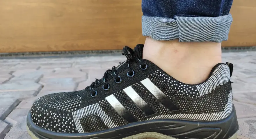 Czarne buty sportowe z białymi paskami i podwiniętymi nogawkami jeansów. Idealny przykład, jak podwinąć spodnie.