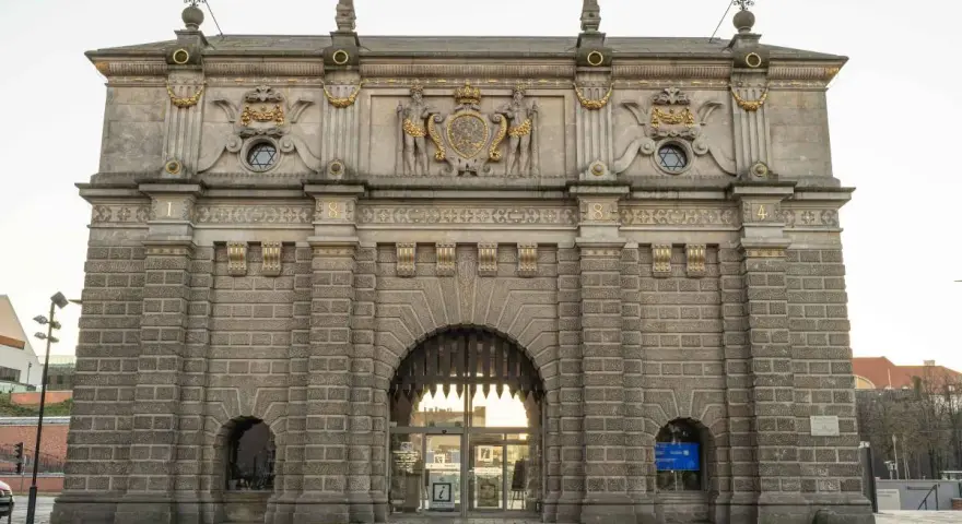 Majestatyczna Brama Wyżynna w Gdańsku, ozdobiona herbem i rzeźbami, zaprasza do zwiedzania.
