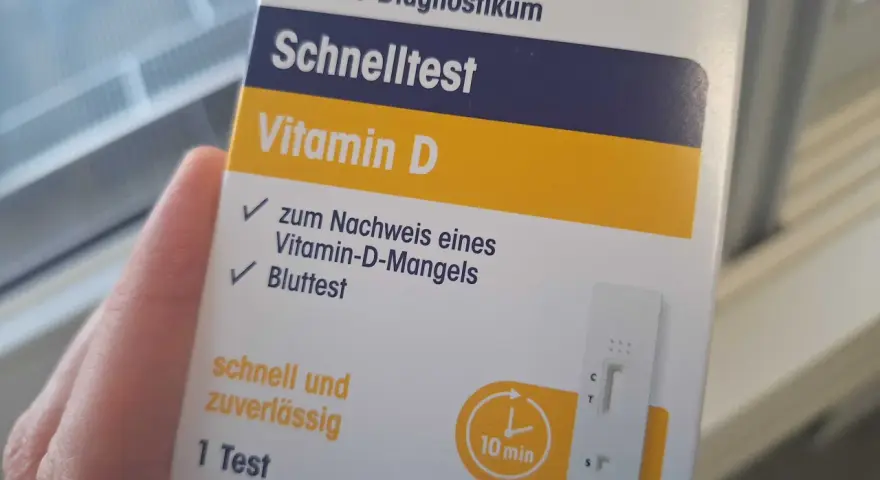 Hand hält eine Verpackung für einen Vitamin-D-Schnelltest mit einem Bluttest-Streifen.