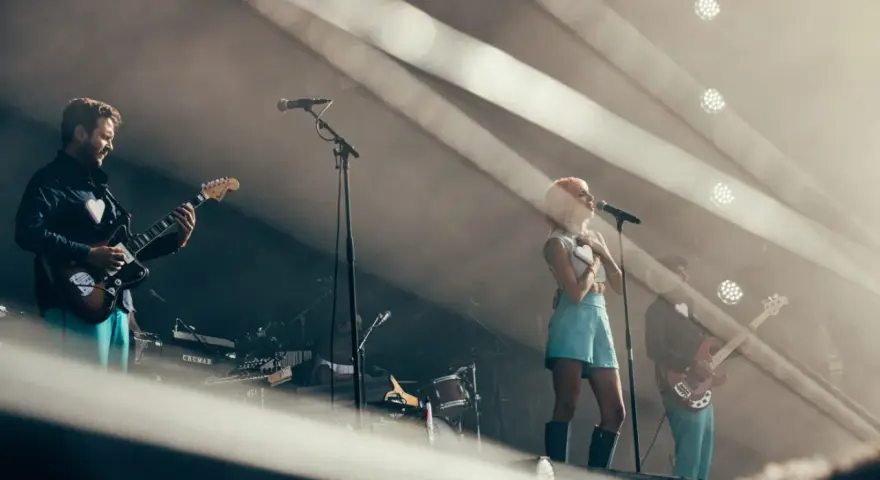 Un groupe de musique sur scène, avec une chanteuse aux cheveux roses et un guitariste. L'ambiance est électrique, typique d'un artiste funk.