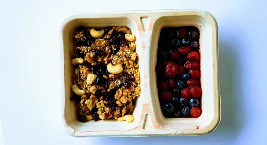 Dwie przegródki pojemnika: jedna z granolą i orzechami, druga z jagodami i truskawkami. Czy kasza jaglana ma gluten? Ta granola wygląda na bezglutenową!