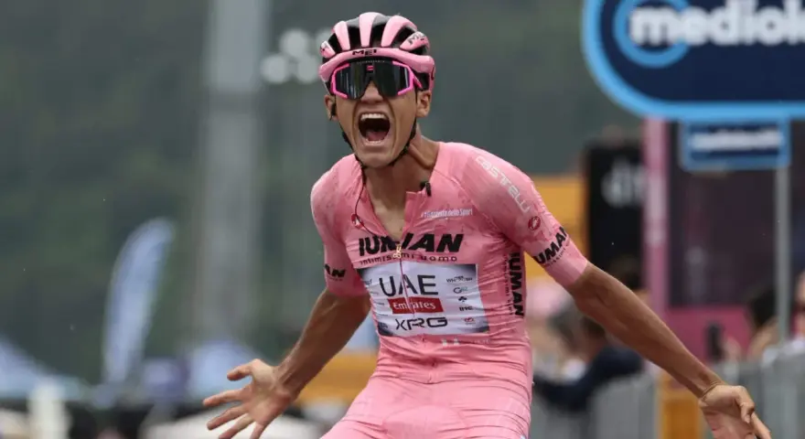 Isaac Del Toro, a cyclist in a pink jersey, screams in triumph, arms outstretched.