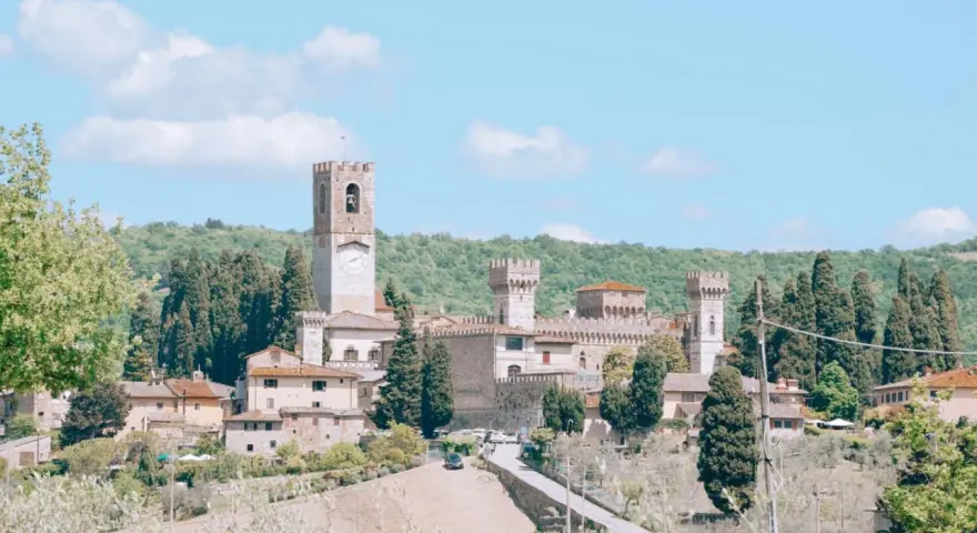 La Badia a Passignano, un borgo medievale toscano con un'imponente torre dell'orologio, circondato da colline verdi e cipressi.
