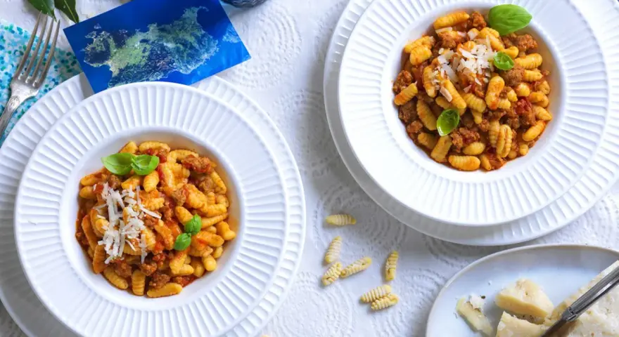 Due piatti di gnocchetti alla campidanese, un assaggio di Sardegna con sugo di salsiccia e pomodoro, guarniti con basilico e parmigiano.