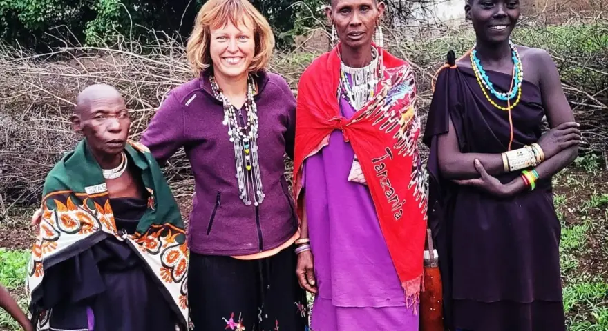 Uśmiechnięta kobieta z Europy wśród ludności Tanzanii. Trzy kobiety z plemienia Masajów w tradycyjnych strojach i biżuterii.