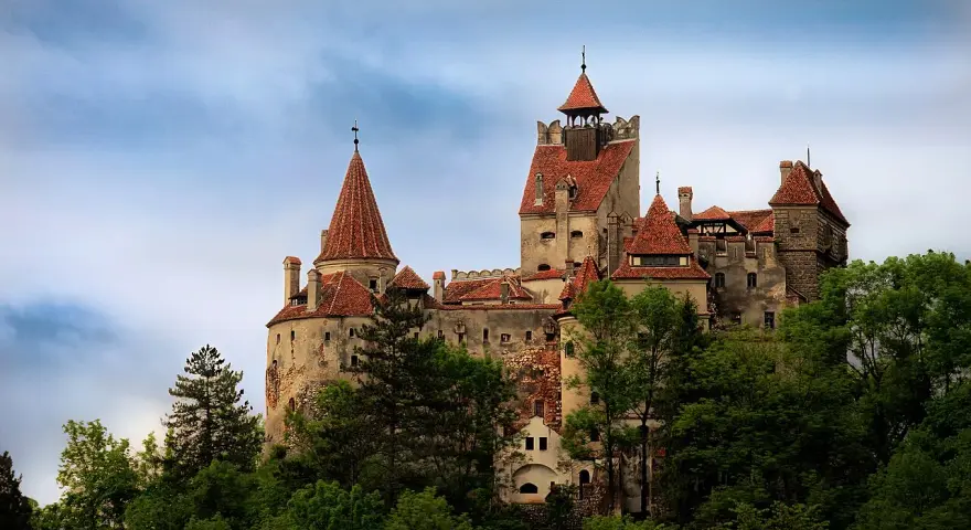 Zamek Bran w Rumunii, otoczony zielenią, z charakterystycznymi wieżami i czerwonymi dachami, wygląda jak z bajki.