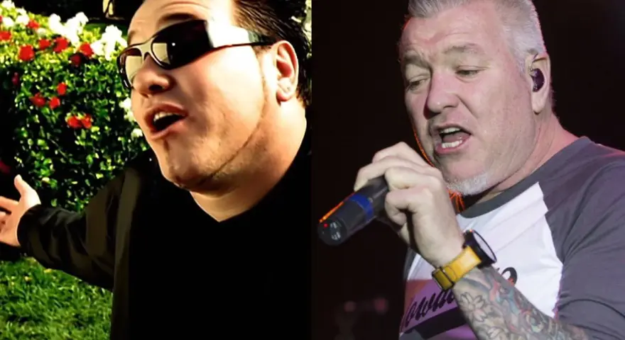 Steven Harwell w okularach przeciwsłonecznych śpiewa na tle ogrodu, obok Steven Harwell z tatuażami trzyma mikrofon na scenie.