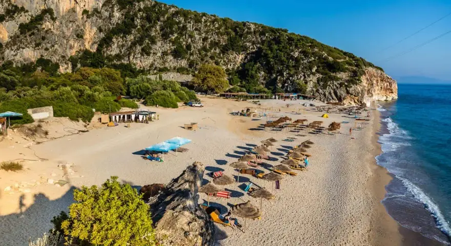 Piękne albania plaże z rzędami parasoli i leżaków, skaliste zbocze i turkusowe morze.