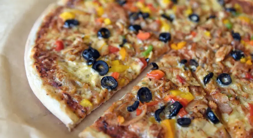 Co to jest pizza? To pyszna, okrągła pizza z oliwkami, papryką i serem, pokrojona na kawałki.