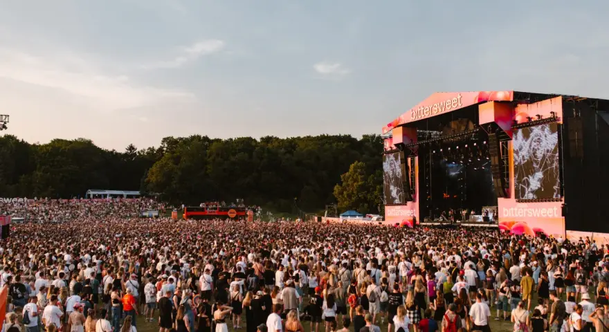 Tłum ludzi na festiwalu Bittersweet 2026, podziwiający scenę z wielkim ekranem i artystami. Słońce zachodzi, tworząc ciepłą atmosferę.