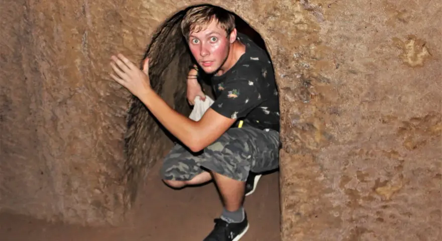 Młody mężczyzna kuca w wąskim tunelu, jednym z historycznych Cu Chi Tunnels.