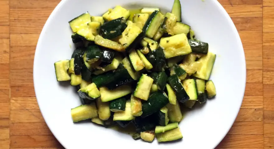 Zucchine in umido, un contorno saporito e leggero, servito in un piatto bianco su un tagliere di legno.