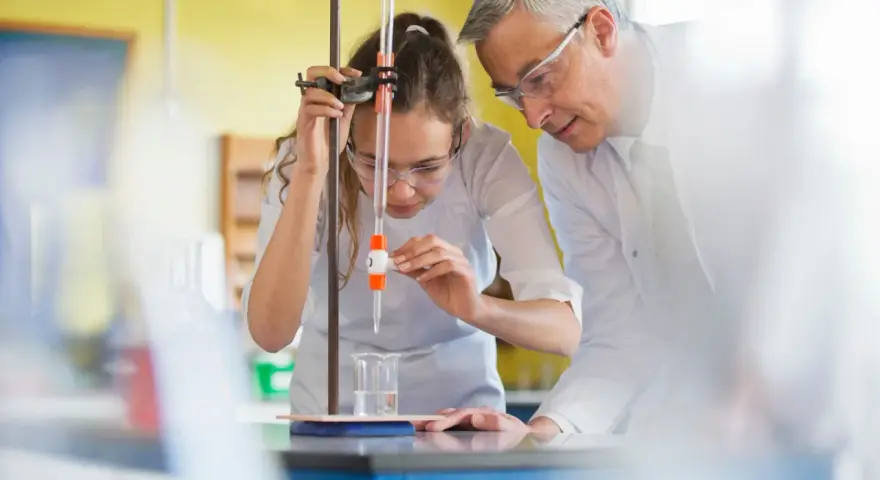 Schülerin bei chemischem Experiment mit Lehrer. Perfekt für die Ausbildung mit Abitur NRW.