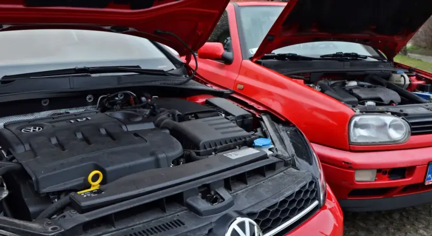 Dwa czerwone Volkswageny z otwartymi maskami. Nowszy model z silnikiem TDI obok starszego, gdzie widać stary diesel.