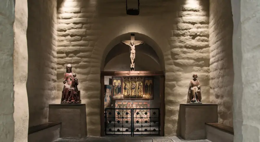 En kyrka från medeltiden med en krucifix, helgonstatyer och altarskåp.