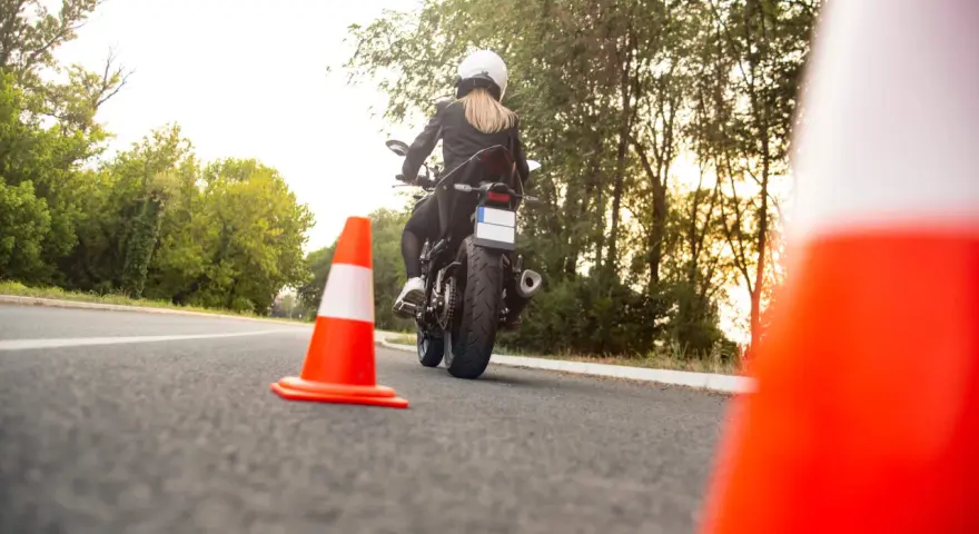 Kobieta na motocyklu podczas egzaminu na prawo jazdy kat A. Sprawdza cenę kursu.