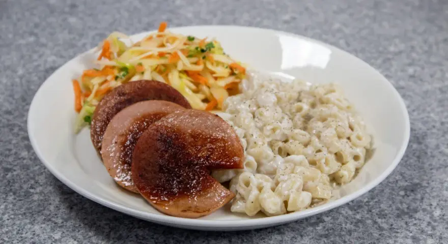 En tallrik med stuvade makaroner, stekt falukorv och en sallad på vitkål och morötter.