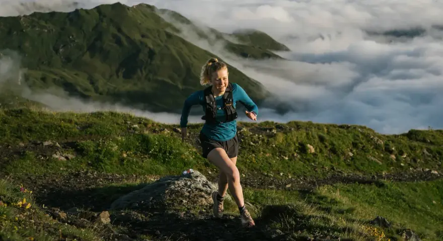 Donna corre su sentiero montano, immersa nella nebbia. Il trail running significato è libertà e sfida.